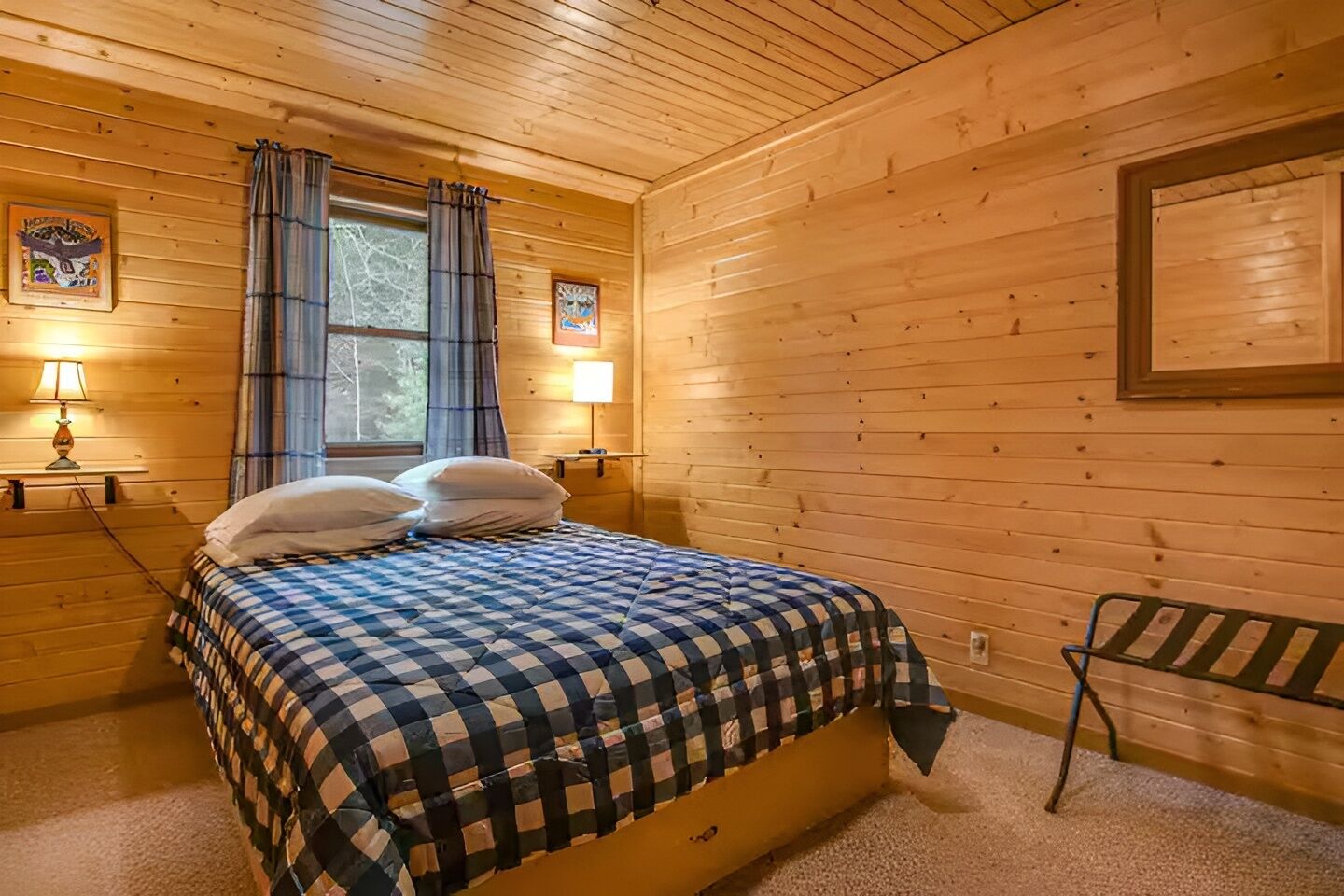 Une chambre à coucher dans un chalet en bois, avec un lit, deux lampes de chevet, une fenêtre avec des rideaux et un tableau encadré au mur.
