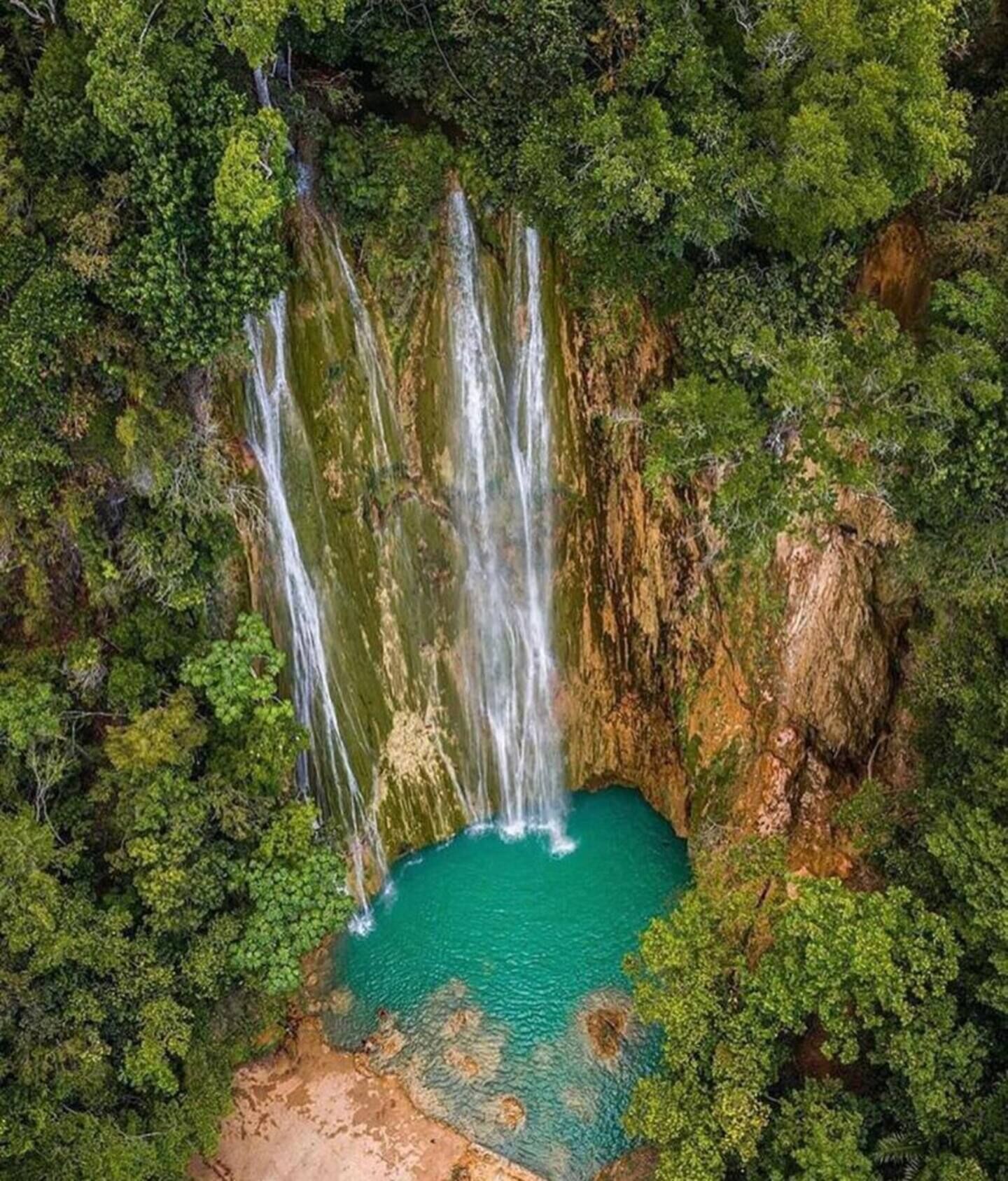 Ein Wasserfall stürzt in ein türkisfarbenes Becken, umgeben von dichtem Grünwald.