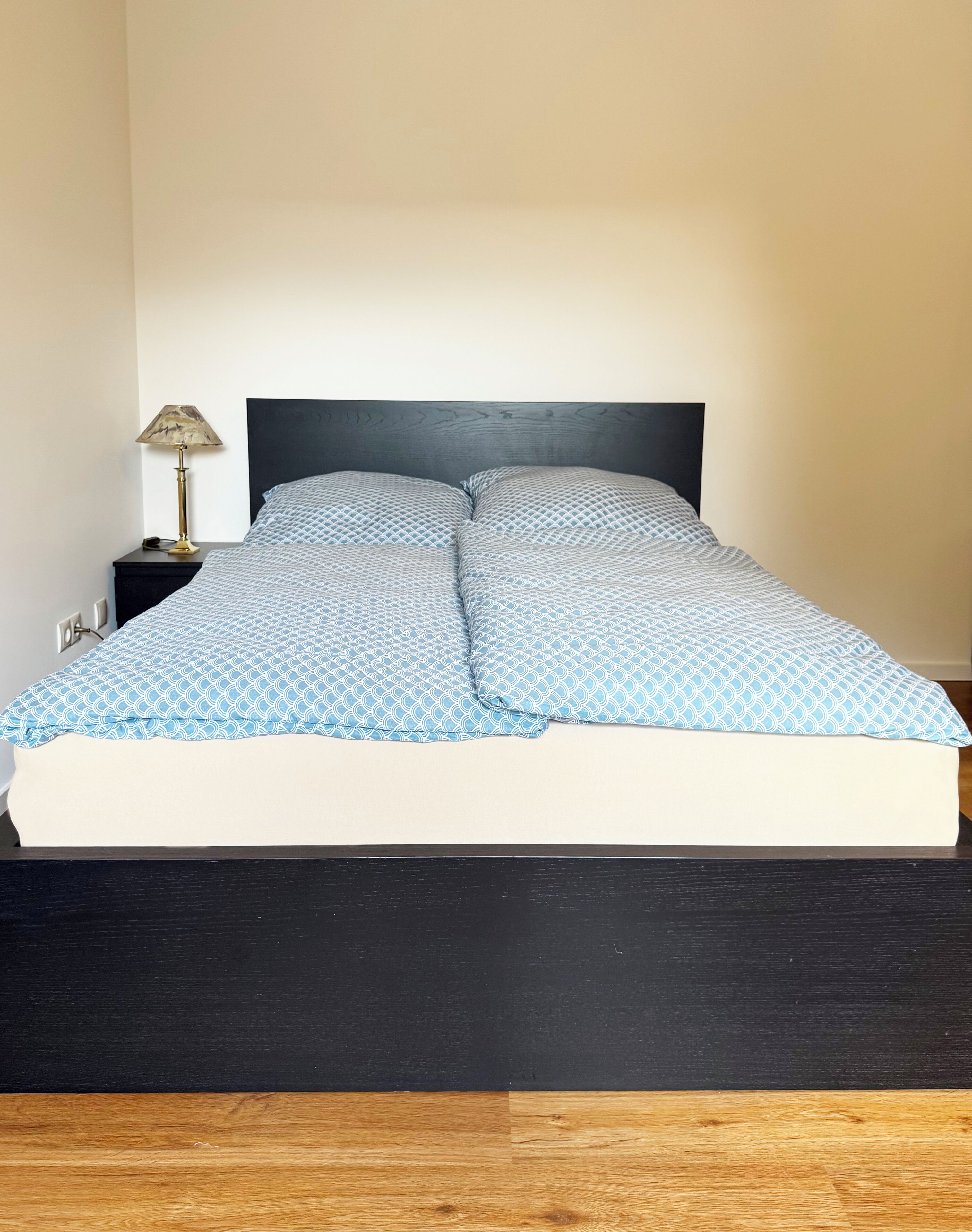 Ein Bett mit einem gemusterten Überwurf, einem schwarzen Kopfteil und einem Nachttisch mit einer Lampe.