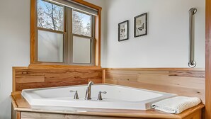 Ein Badezimmer mit einer großen Badewanne, Holzverkleidung, einem Fenster und zwei gerahmten Bildern an der Wand.