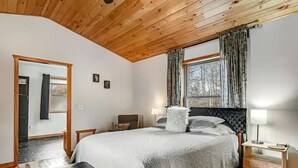 Ein Schlafzimmer mit Holzboden, einem großen Bett mit weißer Bettdecke, zwei Nachttischlampen, einem Nachttisch aus Holz und einem Fenster mit Vorhängen.
