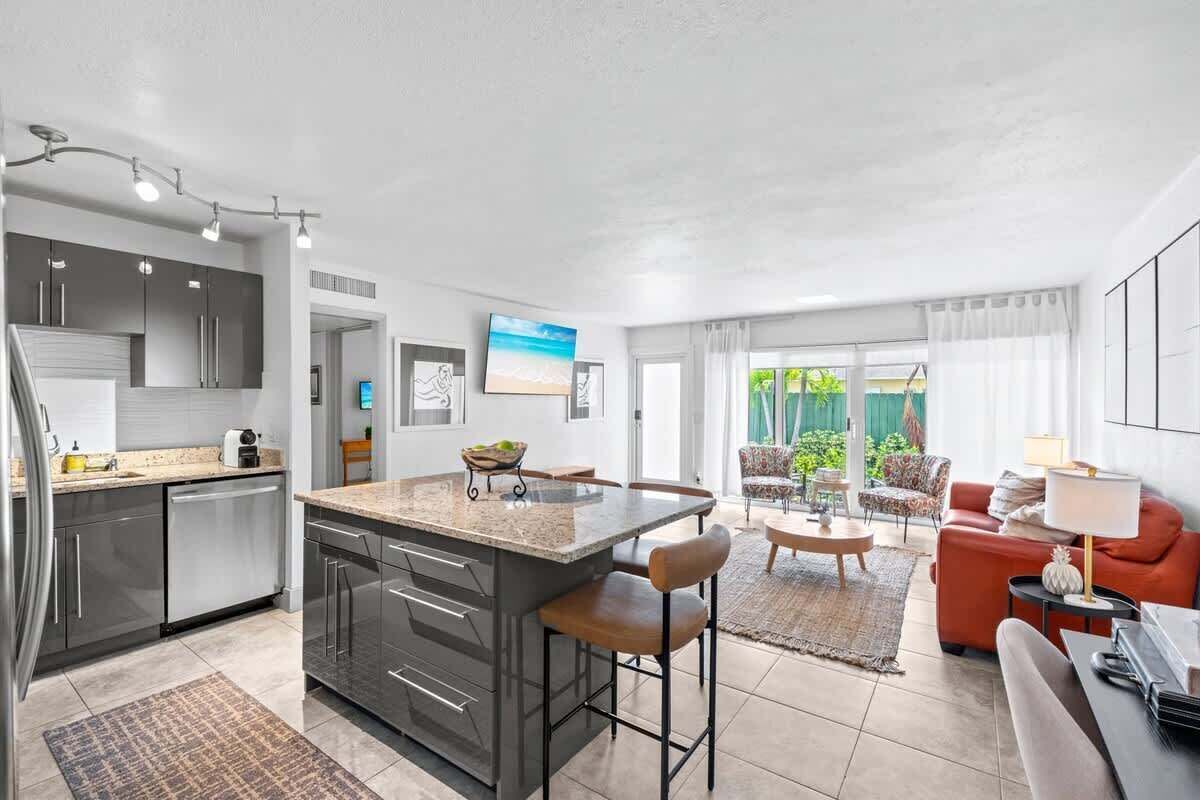 A modern kitchen with a central island, a dining area with a round table, and a living room with a sofa and chairs.