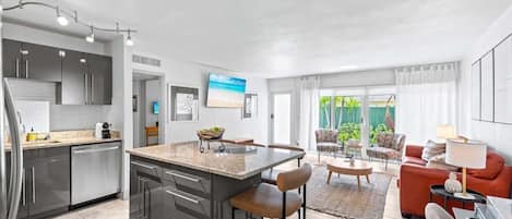 Una cocina moderna con una isla central, un comedor con mesa redonda y una sala de estar con sofá y sillones.