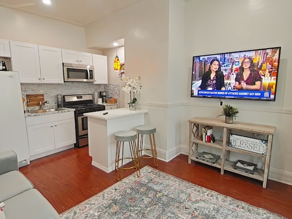 A modern kitchen with white cabinets, a central island, and a flat-screen TV displaying a news broadcast.