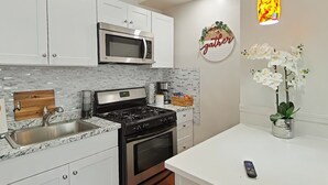 A modern kitchen with white cabinets, a stainless steel microwave, a gas stove, and a sink.