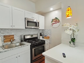 A modern kitchen with white cabinets, a stainless steel microwave, a gas stove, and a sink.