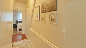 A hallway with a bed, a door, and framed pictures on the wall.
