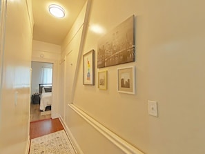 A hallway with a bed, a door, and framed pictures on the wall.