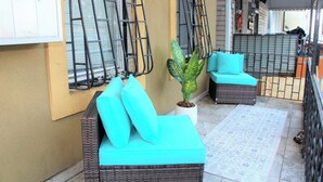 A balcony with wicker furniture, a potted plant, and a tiled floor.