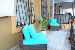 A balcony with wicker furniture, a potted plant, and a tiled floor.
