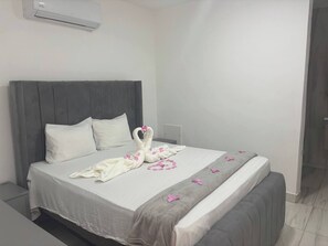 A neatly made bed with a white and gray bedspread, two pillows, and decorative swan-shaped towels with pink flowers. - Charming Studio in Sosúa, Dominican Republic - Perfect Beach Getaway (Sosúa)