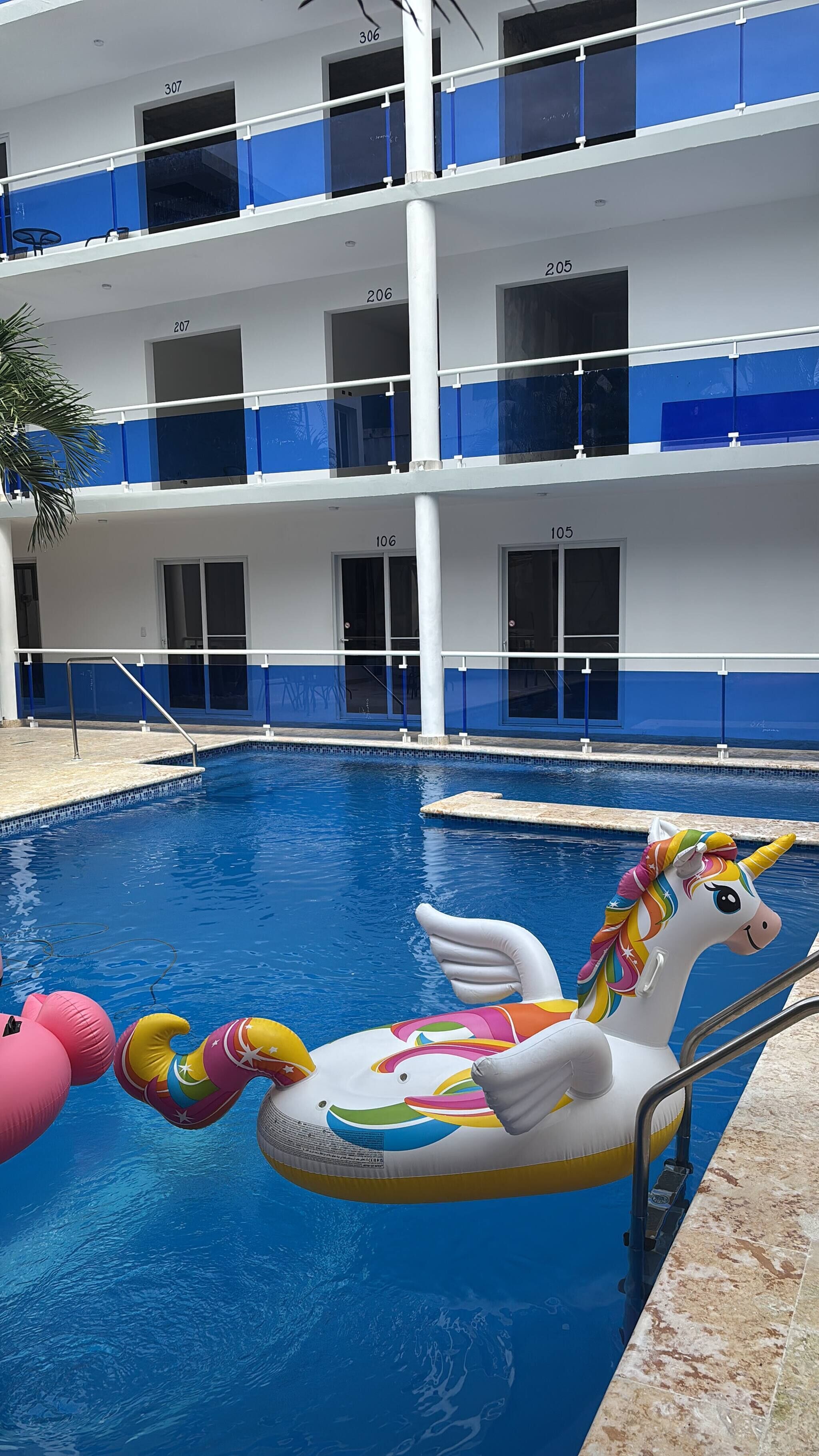 A swimming pool with a unicorn float and other inflatable toys, surrounded by a building with balconies and windows.