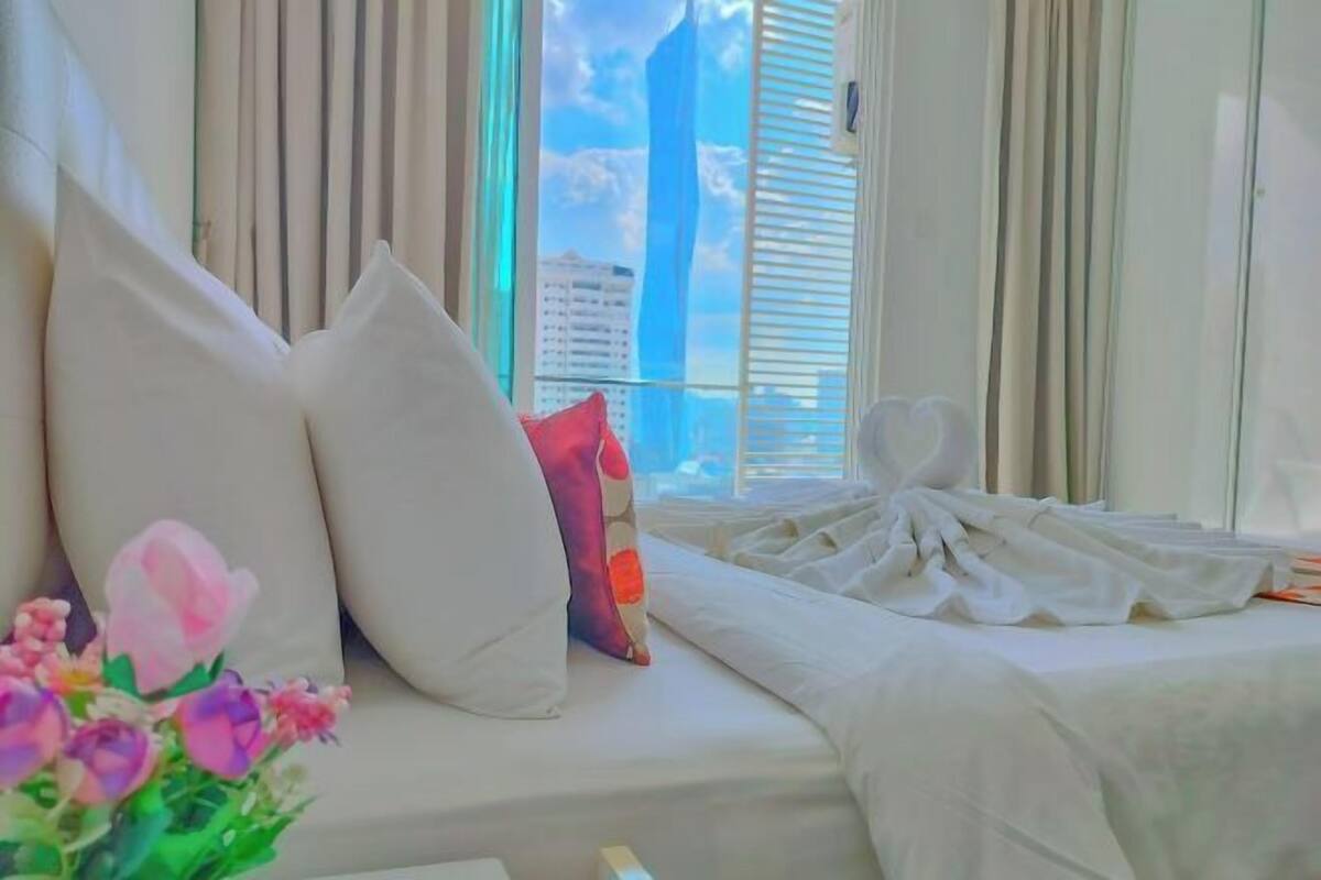 A hotel room with a bed, pillows, a window with blinds, and a view of a building.