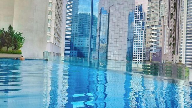 A swimming pool with reflections of surrounding high-rise buildings. - Lila Suite One Bukit Ceylon (Kuala Lumpur)
