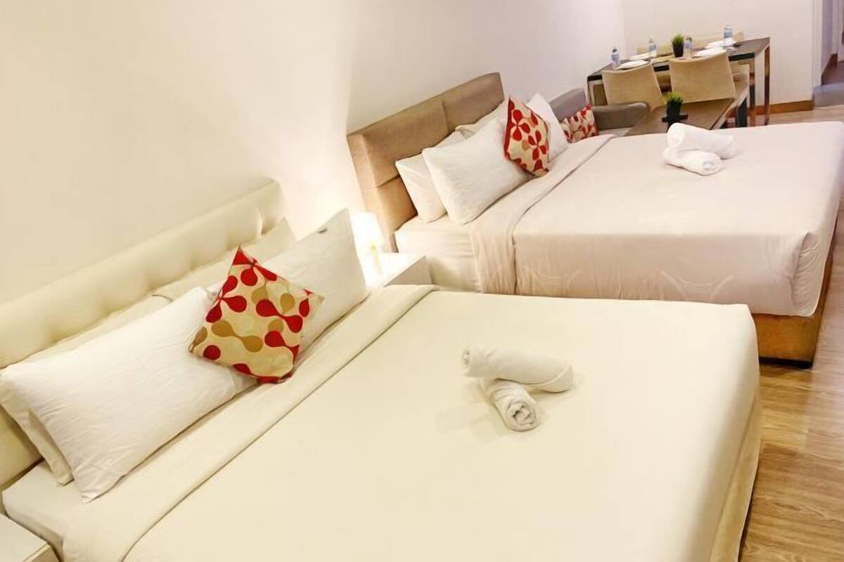 A hotel room with two beds, each with white bedding and a rolled towel. There is a desk with a chair and a small table with a plant.