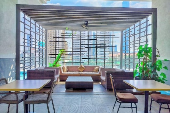 A modern indoor seating area with a sofa, tables, and chairs, featuring large windows and a view of the city. - Lila Suite One Bukit Ceylon (Kuala Lumpur)