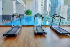 Tres cintas de correr en una sala con pared de vidrio, una piscina pequeña interior y vista a edificios altos.