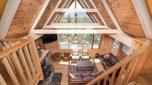 A cozy cabin interior with a stone fireplace, wooden flooring, and a seating area with a brown leather sofa and two chairs. - Bass Lake luxury cabin with lake views & boat slip (Bass Lake)