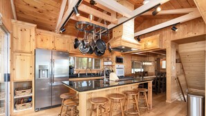 A modern kitchen with wooden cabinetry, stainless steel appliances, and a central island with bar stools. - Bass Lake luxury cabin with lake views & boat slip (Bass Lake)