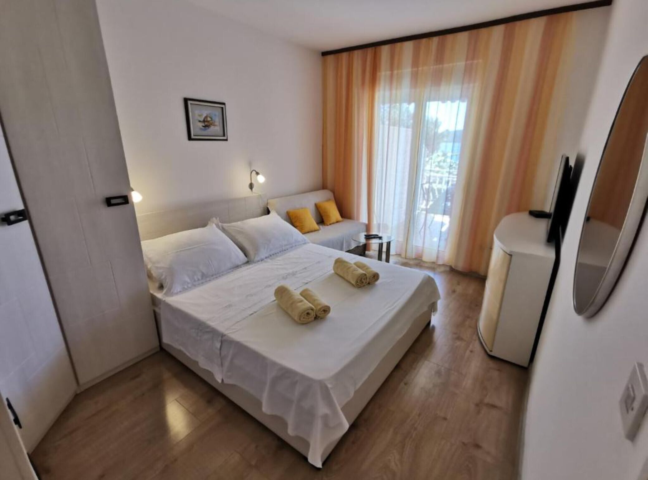 A hotel room with a bed, a small table, a chair, a TV, and a window with curtains.