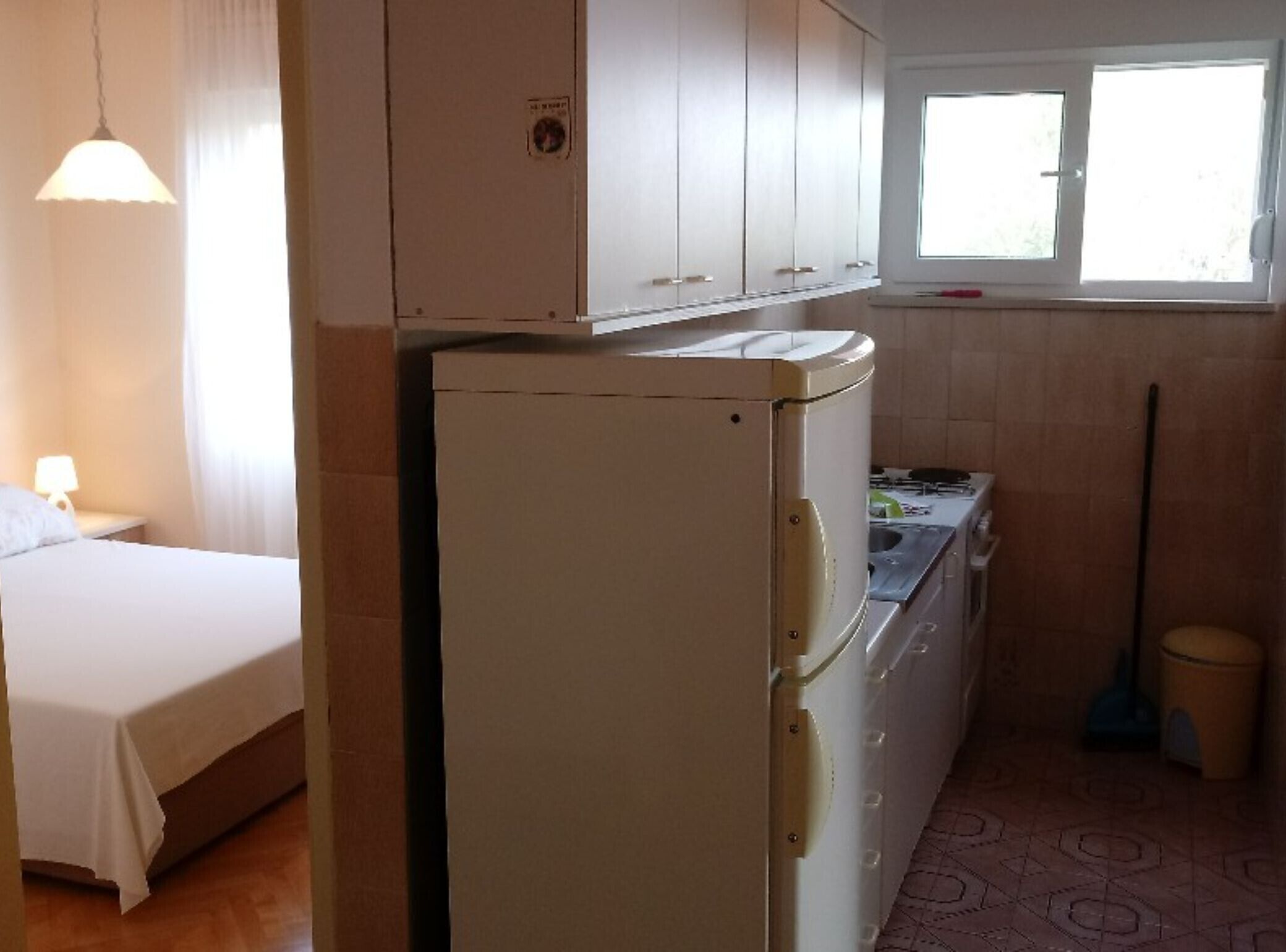 Ein kompaktes Hotelzimmer mit Bett, Küchenzeile, Kühlschrank und einem Fenster mit Vorhängen.