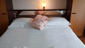 A neatly made bed with white linens and pink accents, a bedside lamp, and a wooden headboard. - Double Room with Garden View and Balcony (Okrug Gornji)