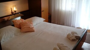 A neatly made bed with towels, a bedside lamp, and a window with sheer curtains. - Double Room with Garden View and Balcony (Okrug Gornji)