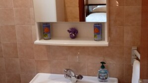 A bathroom with a white sink, a mirror, and a shelf with toiletries. - Double Room with Garden View and Balcony (Okrug Gornji)