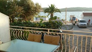 A balcony with a glass table and chairs, overlooking a body of water and a road with vehicles. - Double Room with Garden View and Balcony (Okrug Gornji)