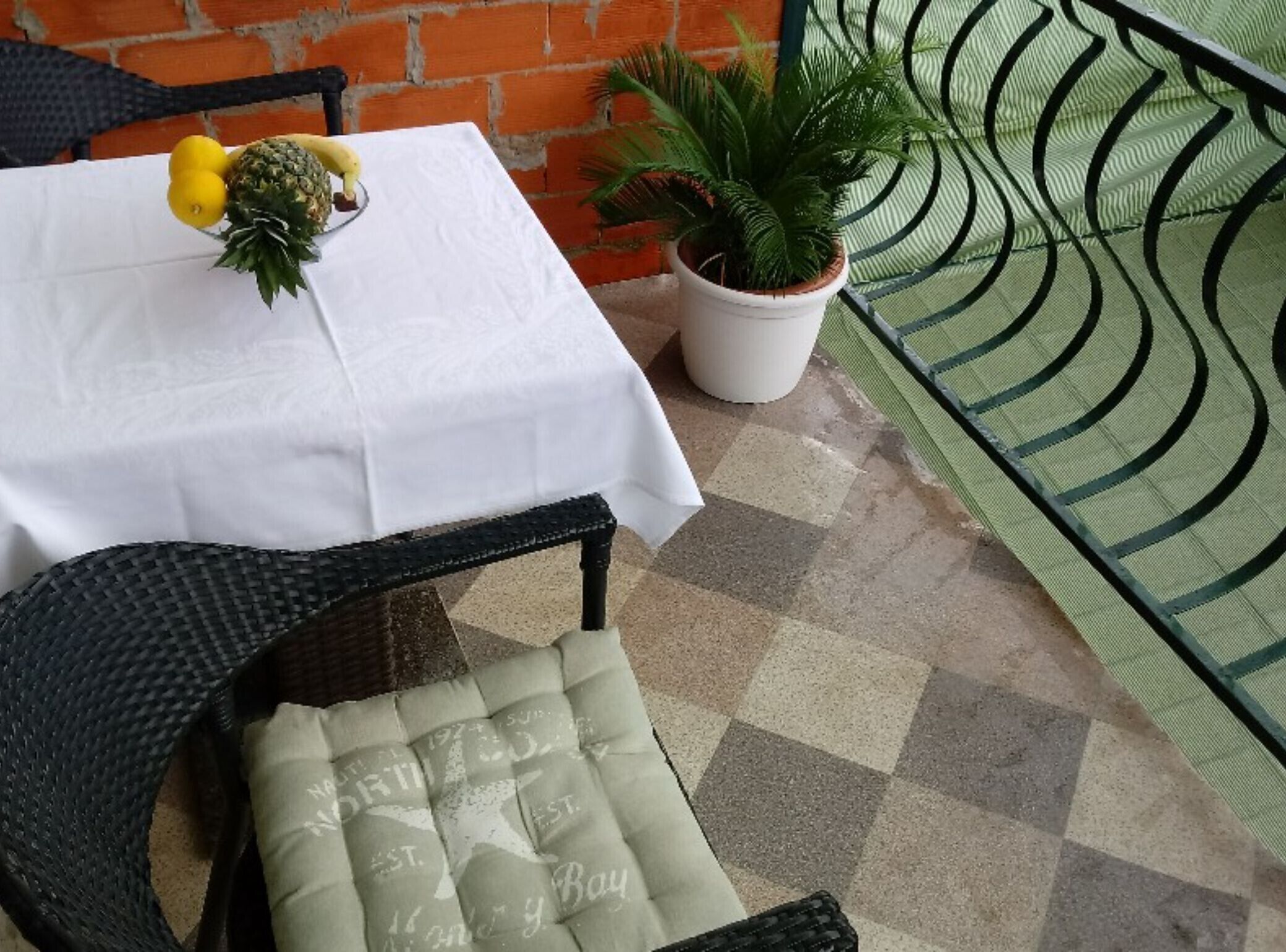 A table with a white tablecloth, a chair with a cushion, a potted plant, and a metal railing.