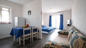 A room with a bed, a sofa, a table with a blue tablecloth, a chair, a TV, and a window with curtains.