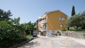 A yellow building with a balcony, surrounded by greenery and a stone wall.