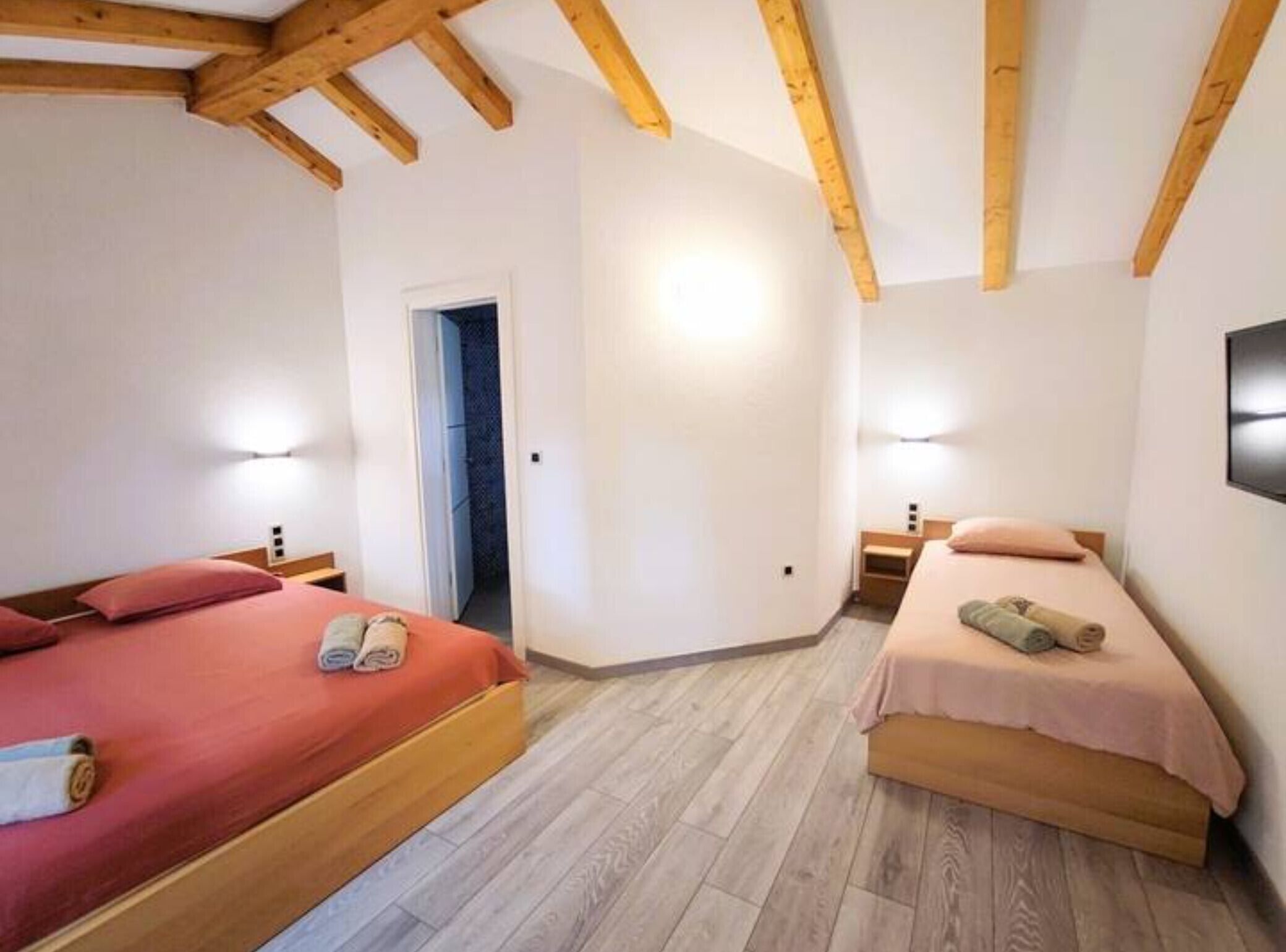 A room with two beds, wooden beams on the ceiling, and a door leading to another room.