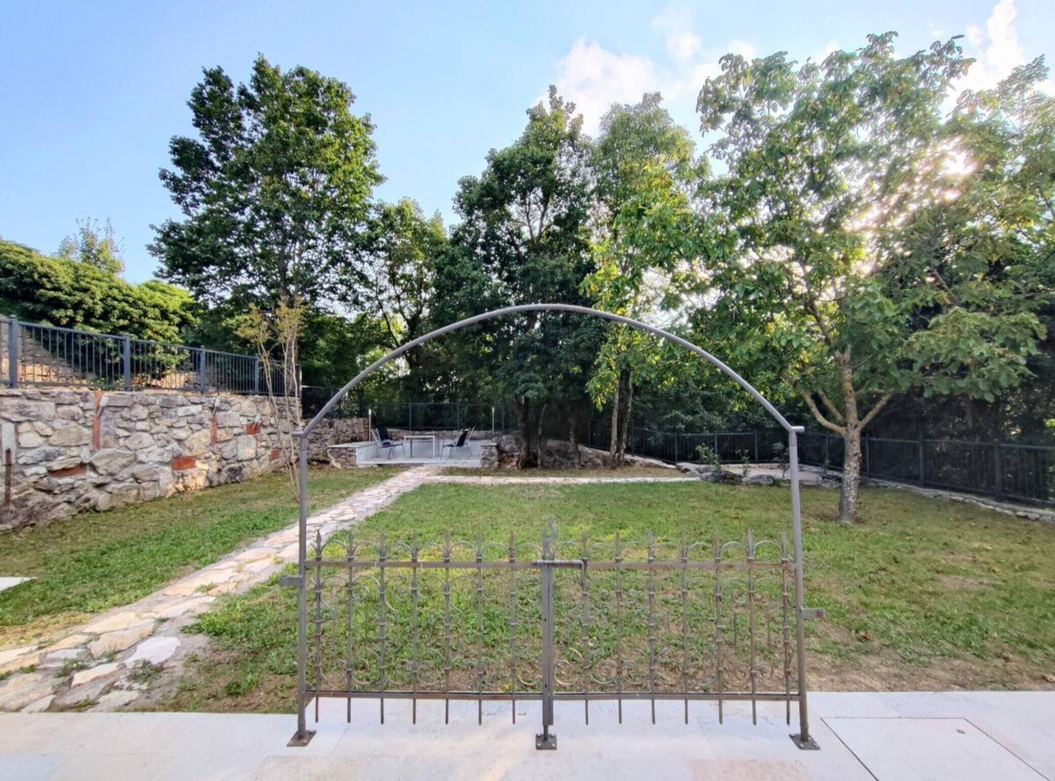 Un muro de piedra, una reja metálica y un sendero pavimentado en un parque.