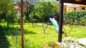 Un jardin avec un toboggan, une pergola en bois et un espace clos agrémenté de plantes.