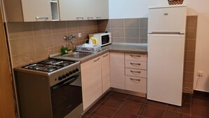 Une cuisine compacte équipée d’une cuisinière à gaz, d’un four, d’un four à micro-ondes et d’un réfrigérateur blanc.