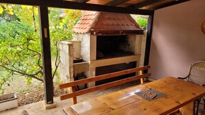 Un espace barbecue extérieur avec un four en pierre, une table en bois et des chaises.