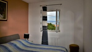 A bedroom with a bed, a radiator, a window with curtains, and a view of the outside.