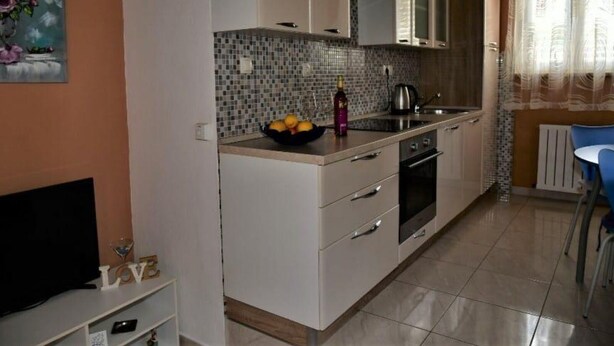 A modern kitchen with white cabinets, a tiled backsplash, and a dining area with a blue chair.