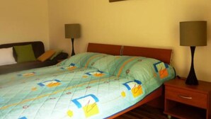 A bedroom with a bed, two bedside tables, a nightstand, a wall-mounted lamp, and a framed picture.