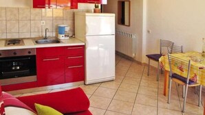 A compact kitchen with red cabinets, a white refrigerator, and a dining area with a table and chairs.