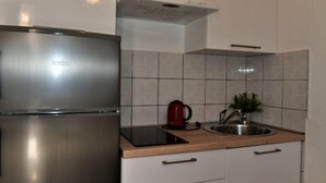 A modern kitchen with a stainless steel refrigerator, a built-in oven, a sink, and a countertop with a red kettle and a plant.
