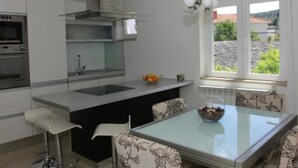 Une cuisine moderne dotée d’un îlot central, d’un coin repas avec une table en verre et d’une vue sur un paysage rocheux, visible à travers une fenêtre.
