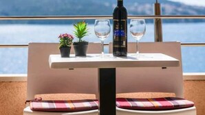 Una mesa con una botella, dos vasos, dos plantas en macetas y vista al mar.