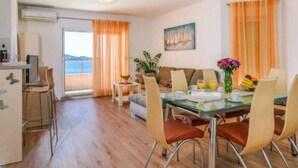 Un comedor con una mesa de vidrio, cortinas naranjas y vista al mar.