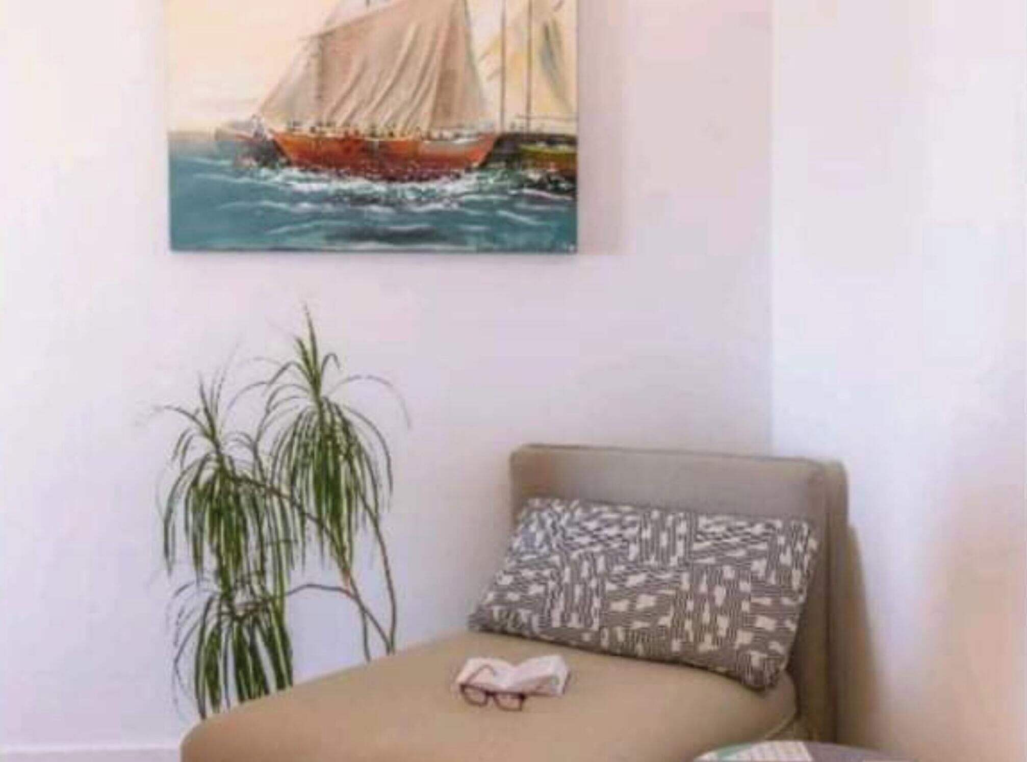 Ein Zimmer mit einem Bett, einem Kissen, einer Pflanze und einem Gemälde eines Segelboots an der Wand.