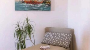 Una habitación con una cama, un almohadón, una planta y un cuadro de un velero en la pared.