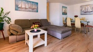Una sala de estar moderna con un sofá modular, una mesita blanca con un florero y un comedor con mesa de vidrio y sillas.