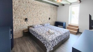 A bedroom with a stone wall, a bed with a floral bedspread, a wooden bench, and a window with a view. - Villa Galant with Pool & Sauna Maružini (Kanfanar)