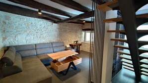 A modern living room with exposed wooden beams, a stone wall, a sofa, a wooden coffee table, and a staircase. - Villa Galant with Pool & Sauna Maružini (Kanfanar)